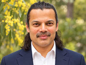 Hitendra Joshi standing in front of a wattle tree and greenery