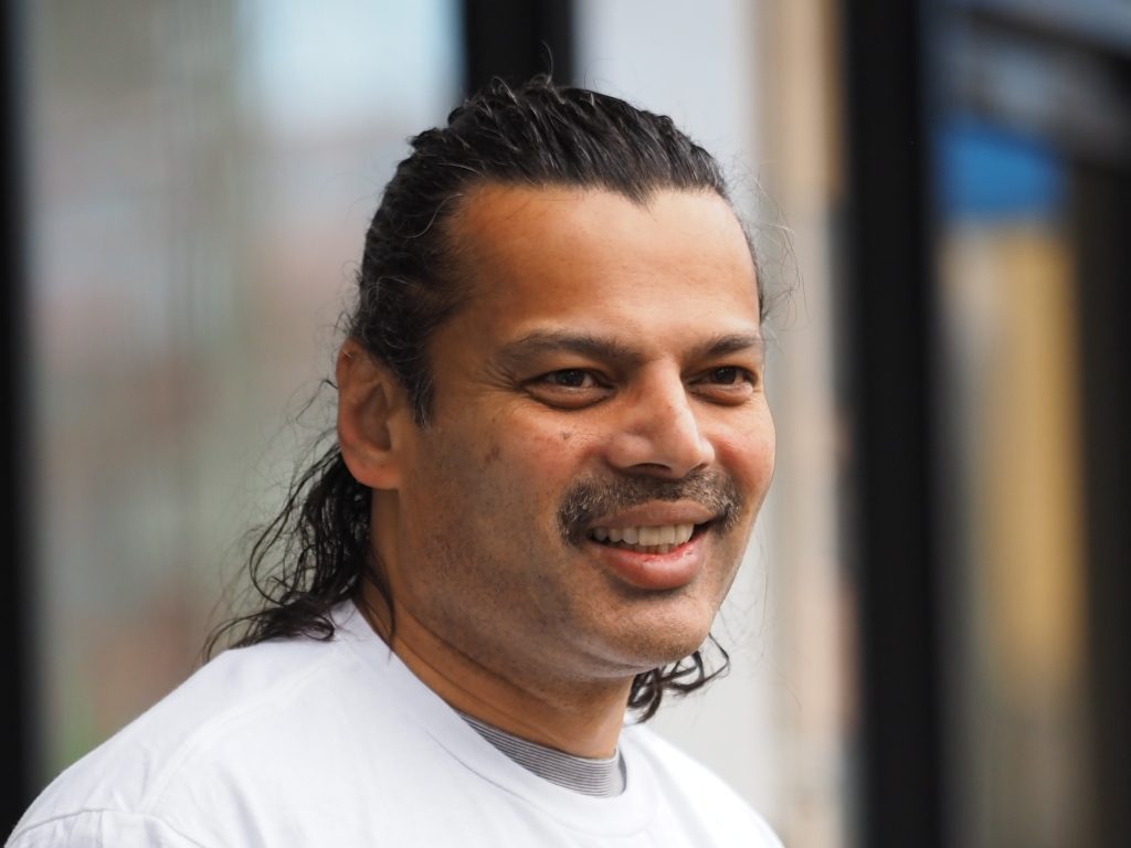 Hitendra Joshi smiling, in a white T-shirt on a shopping street
