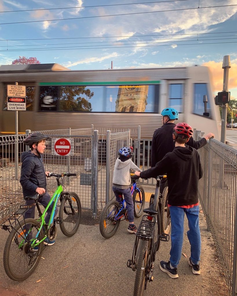 Photo of a family with their bicycles, waiting for the train to pass at a railway crossing in Guildford. Photo by Emily Wilson Photography.